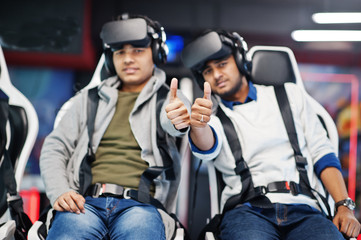 Fototapeta na wymiar Two young indian people having fun with a new technology of a vr headset at virtual reality simulator. They happy and show thumb up.