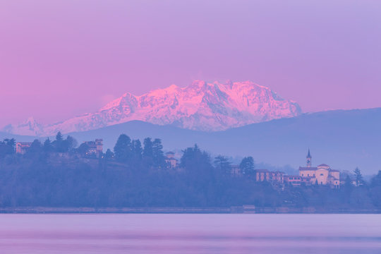 The first lights at sunrise on the church of Biandronno and Monte Rosa from lake Varese. Varese, Lake District, Lombardy, Italy.