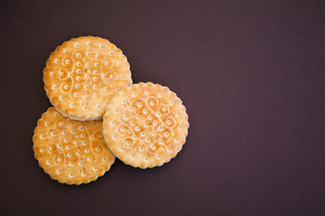 Three cookies on a chocolate (dark brown) ground