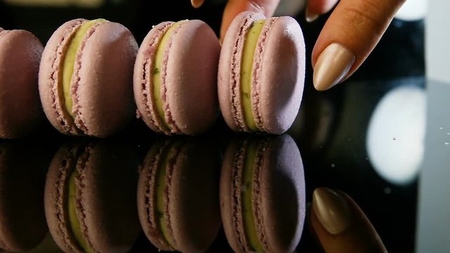 human hand takes away one by one violet macaroon from one row