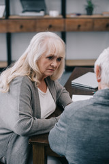 sad senior woman in casual clothes sitting at table with man at home