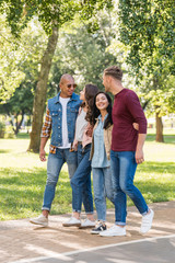 smiling multiethnic friends hugging while walking together in park