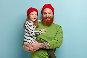 Cheerful stylish father with foxy beard holds little smiling daughter on arms have fun, play together, pose for making family portrait, have ginger hair, look similar. Parents, children, relationship