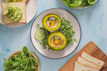 Healthy vegan breakfast. Diet. Baked avocado with egg and fresh salad from arugula, toast and butter. On a white marble plate, a light concrete table. A cup of coffee. Copy space