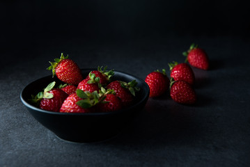 Strawberries in dark bowl with dark background, copy space, side view selective focus