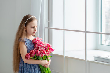 Portrait of a beautiful blue-eyed girl, a little girl among spring flowers in a bright room.