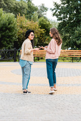 Obraz premium happy girls in sunglasses smiling while looking at each other and talking in park