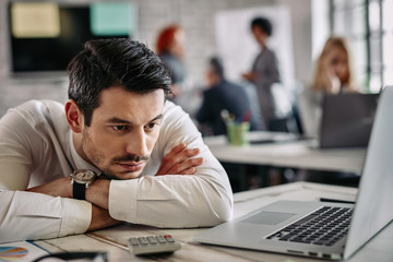 Pensive businessman feeling bored after working on laptop in the office.