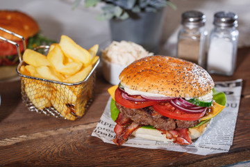 Fresh classic burger with beef, cheese, bacon, onion and lettuce in bun with poppy seeds on wooden table.