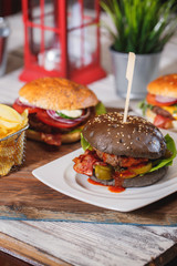 Fresh classic burger with beef, cheese, bacon, onion and lettuce in dark bun on wooden table.