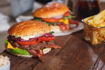 Two fresh classic burgers with beef, cheese, bacon, onion, tomato and arugula on wooden table.