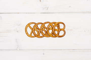 Lot of whole mini salted pretzels in a line flatlay on white wood