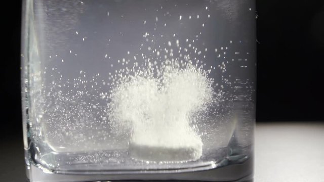 Effervescent antacid tablet in glass of water on black background with rotating