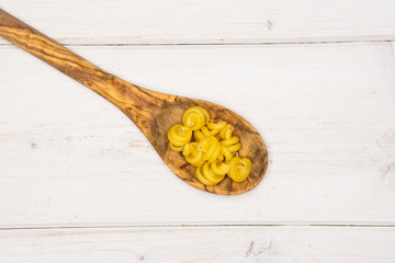Lot of whole raw pasta funghetto variety in a wooden spoon flatlay on white wood
