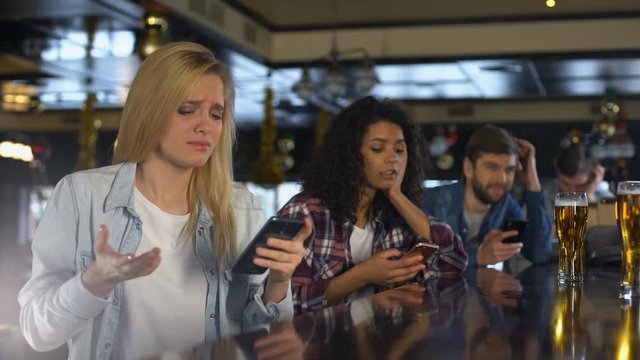 Young women in bar checking sport bets in cellphone, upset about lost money
