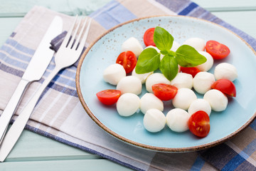 Delicious caprese salad with ripe cherry tomatoes and mini mozzarella cheese balls with fresh basil leaves.