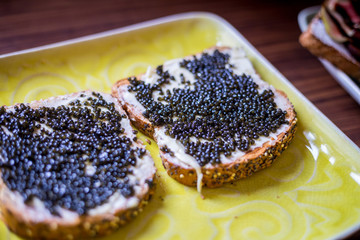 Sandwiches with Black Caviar on the Yellow Rustic Plate, Top View