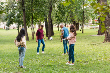 Fototapeta premium cheerful multicultural group of friends standing in park near football