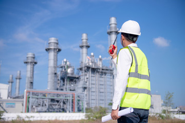 Industrial engineer standing in front of a large  Power plant with safety helmet with gas turbine industry plant background