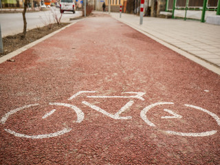 Red bicycle path near roadside, focus on the foreground, passing car.