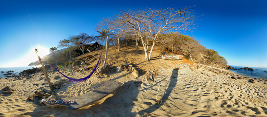 Panoramic view of beautiful tropical private beach with hammock projecting shadow on sand.