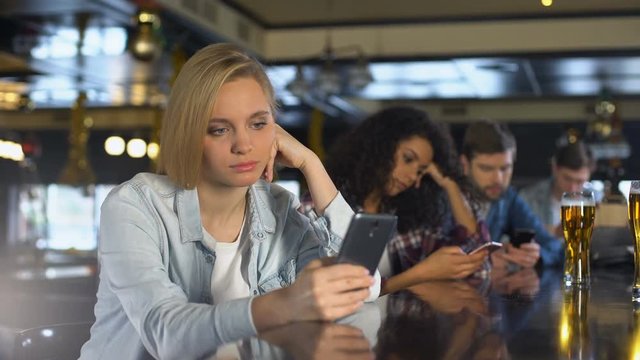 Young people bored in bar, using phones instead of live communication, addiction