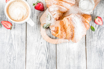 Breakfast concept with coffee cup, croissants, cream and fresh berries. On a light wooden background, top view, copy space
