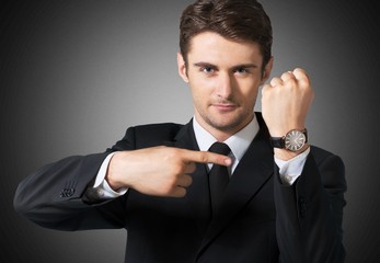Businessman pointing at hand watch on grey wall background, close-up
