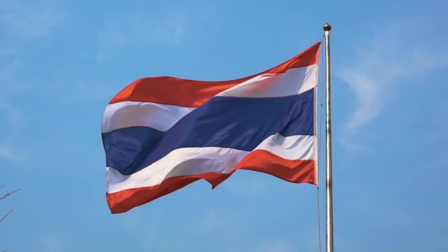 The national flag of Thailand has three colors, consisting of red, white and blue on the flagpole with the wind blowing and having a sky background. slow motion