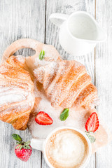 Breakfast concept with coffee cup, croissants, cream and fresh berries. On a light wooden background, top view, copy space