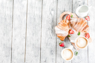 Breakfast concept with coffee cup, croissants, cream and fresh berries. On a light wooden background, top view, copy space