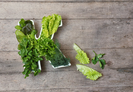 Vitamin K in food concept. Plate in the shape of the letter K with different fresh leafy green vegetables,  lettuce, herbs on wooden background. Flat lay or top view