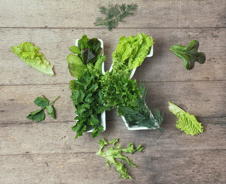 Vitamin K in food concept. Plate in the shape of the letter K with different fresh leafy green vegetables. Some   lettuce and herbs lie near on wooden background. Flat lay or top view