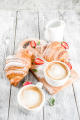 Breakfast concept with coffee cup, croissants, cream and fresh berries. On a light wooden background, top view, copy space