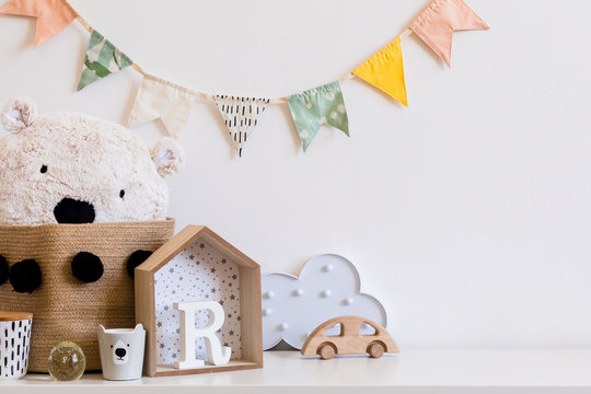 Stylish scandinavian child room with hanging cotton colorful flags on the white wall,  boxes, teddy bear in natural basket, toys.  wooden accessories and cloud. Real photo. Copy space for inscription.