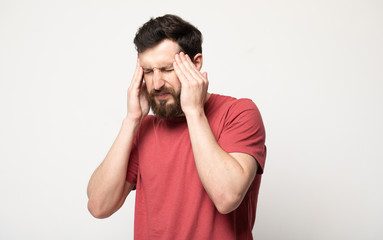 Feeling terrible headache. Portrait of young bearded man is standing and touching his temples while suffering from pain. He is frowning while keeping eyes closed 