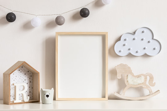 The modern scandinavian newborn baby room with mock up photo frame, wooden toys and children's cup. Hanging cotton lamps and white cloud. Minimalistic and cozy interior with white walls. Real photo.