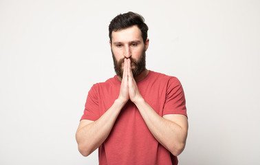 Picture of young guy dressed casually isolated on grey background, having put hands together in...