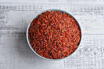 Fototapeta na wymiar Bowl with uncooked red rice on wooden background, top view