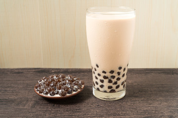A glass cup of pearl milk tea (also called bubble tea) and a plate of tapioca ball on wooden background. Pearl milk tea is the most representative drink in Taiwan. Taiwan food . With copy space.