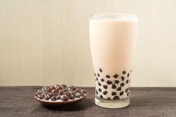 A glass cup of pearl milk tea (also called bubble tea) and a plate of tapioca ball on wooden background. Pearl milk tea is the most representative drink in Taiwan. Taiwan food . With copy space.