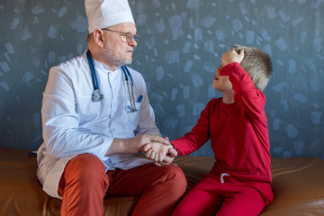 Home doctor in white coat, cap and glasses with gray beard examines two children teenagers at home....
