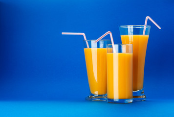 Glasses of orange juice on blue background with copy space