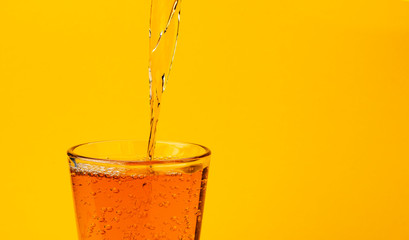 Apple juice pouring into glass, isolated on yellow color background, with copy space