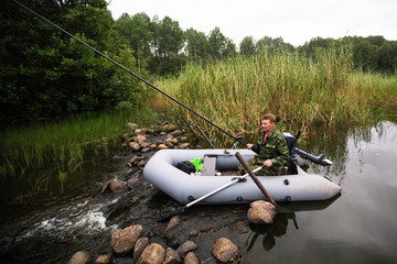 Fisherman on rubber boat catching fish in summer river.  .