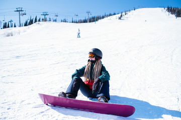 Young woman snowboarder sitting on a snowy slope.