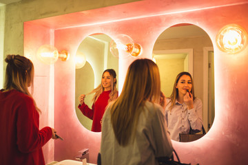 Attractive happy women applying makeup in the bathroom of a restaurant