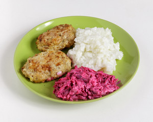 Cutlets, boiled rice and chopped beets on a plate on a white background.
