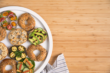 Stylish and tasty composition of vegan bagels sandwiches on the salver with vegetables, herbs, paste, seeds, hummus and lettuce on the brown wooden table. Fresh and healthy breakfast. Copy space.