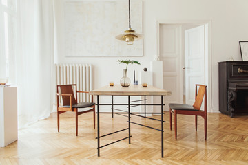 Eclectic and elegant dining room interior with design sharing table, chairs, gold pedant lamp, abstract paintings, piano and stylish accessories. Eclectic decor. Brown wooden parquet. Real photo.